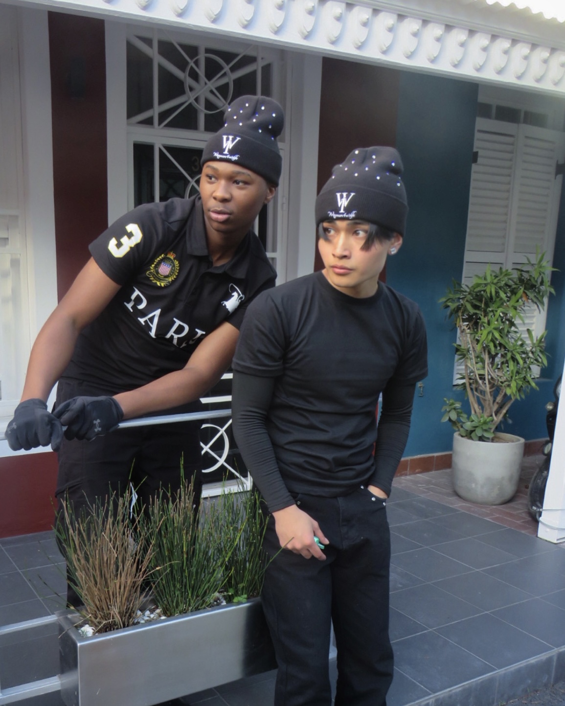 Two people wearing black WANOFWAN beanies beside a street planter