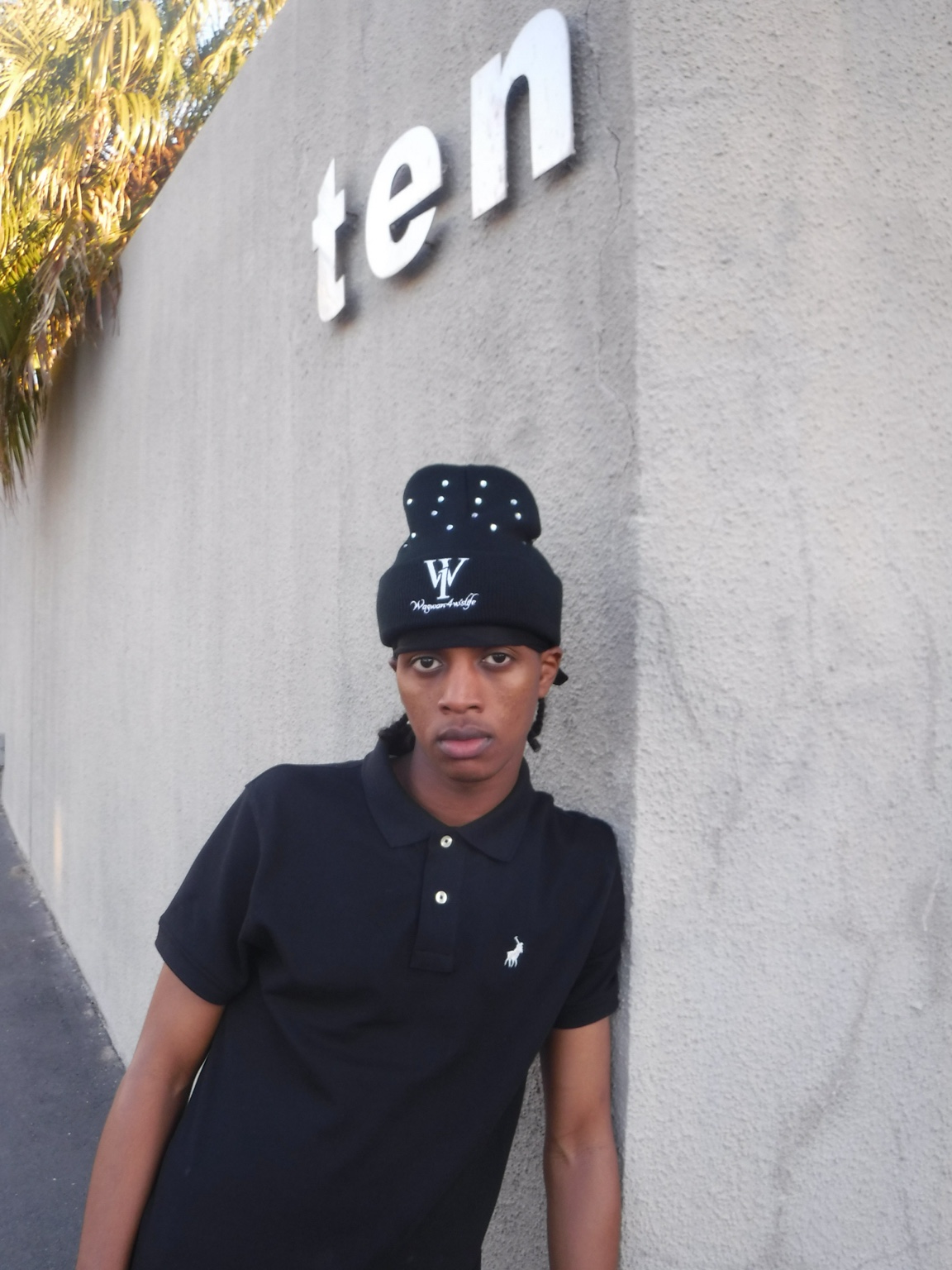 Portrait of a person wearing a black WANOFWAN beanie beside a wall