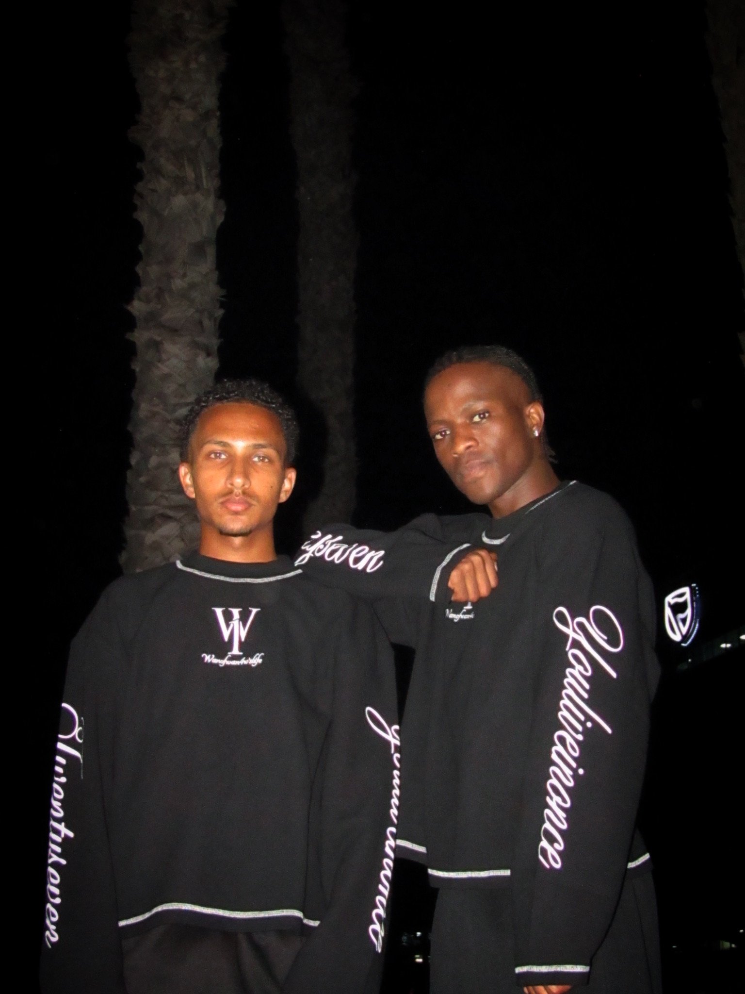 Two models in black WANOFWAN tops showing sleeve graphics